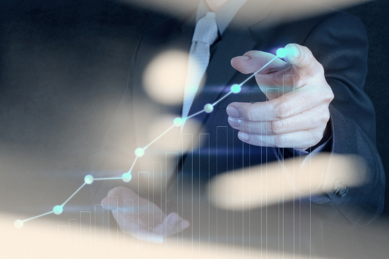 Businessman in a suit pointing at a graph displayed on a screen, illustrating data trends in a professional setting.