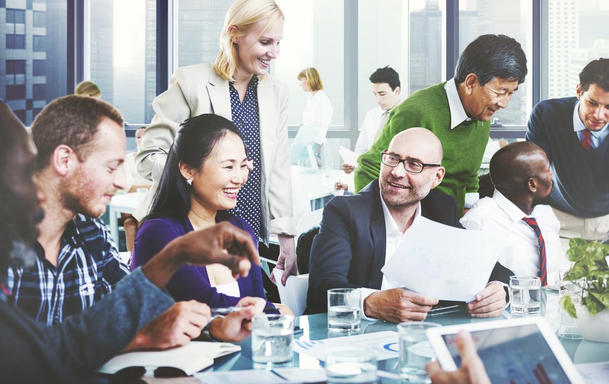 A diverse group of people gathered around a table, collaborating with a laptop open in front of them.