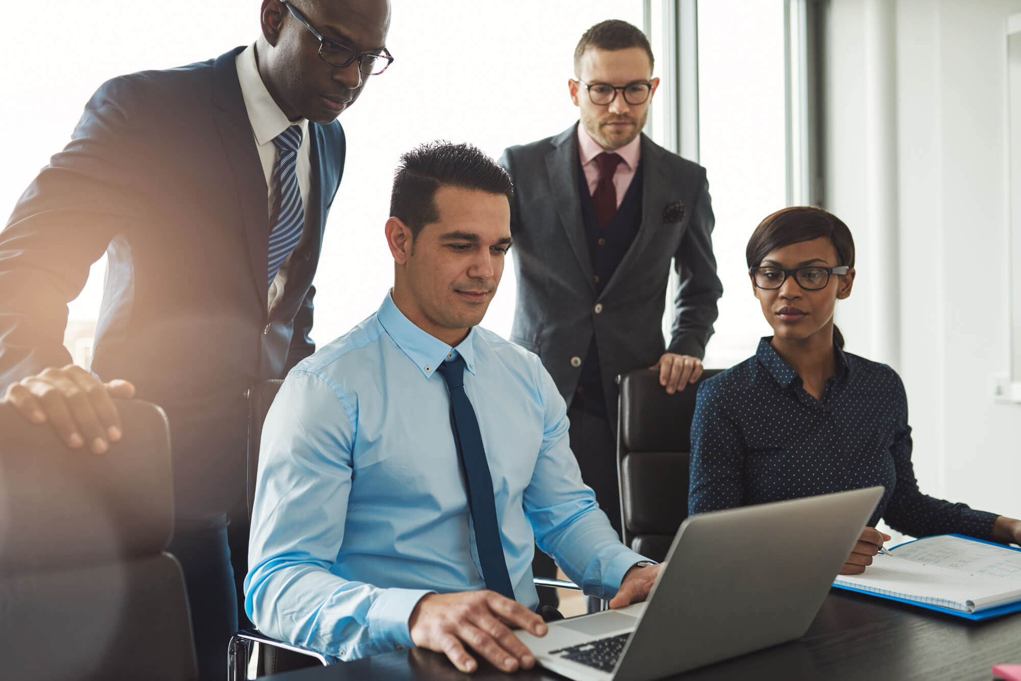 A group of business professionals collaborating on a laptop in a modern office setting.